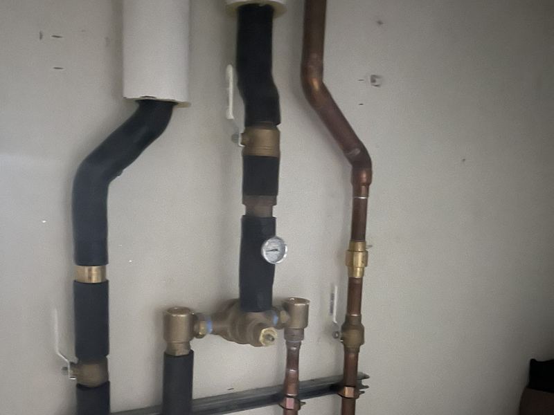 Close-up of a copper water manifold with brass shutoff valves and a pressure gauge