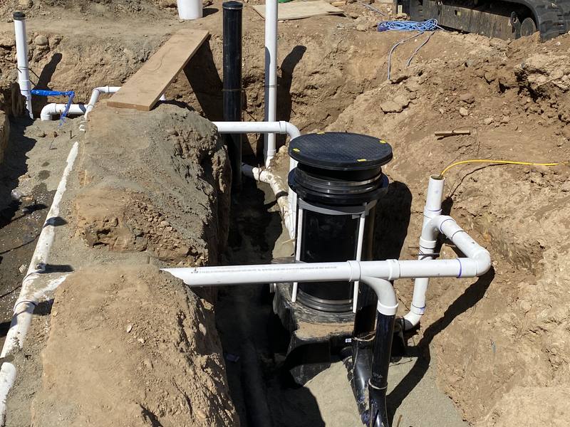 New construction sewer rough-in with PVC drain lines and a cleanout riser set in an open trench