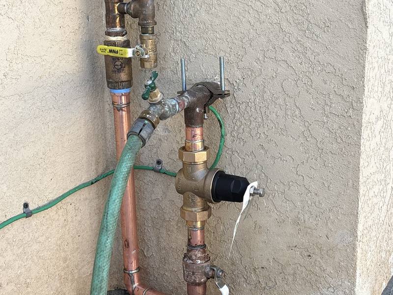 Exterior copper piping with a pressure regulator and hose bib on a stucco wall