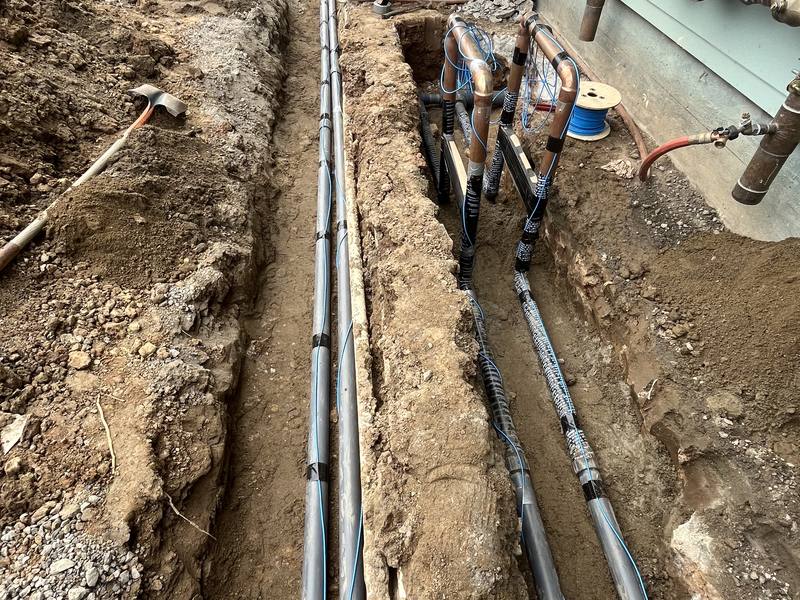 Copper water lines run through a trench alongside a home during a repipe